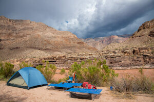Tent and cots on a Grand Canyon beach with storm clouds behind.