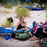 A person missing a leg laughs with friends while sitting on a cot.