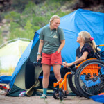 A woman in a wheelchair laughs with a fellow passenger in camp.