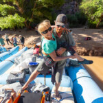A river guide carries a paralyzed woman on the raft.