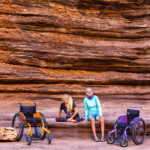 Two paralyzed women smiling while out of their wheelchairs.