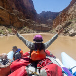 A paralyzed woman raises her arms in the air while on the raft.